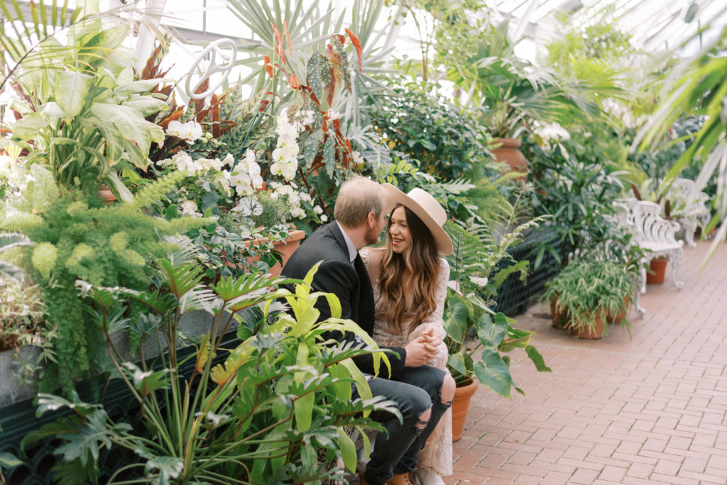Engaged couple sitting on bench inside The Biltmore Conservatory