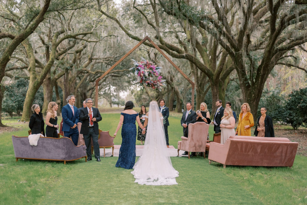 Bride walking down the aisle to her groom on the Avenue of Oaks at Legare Waring House for during intimate micro wedding ceremony