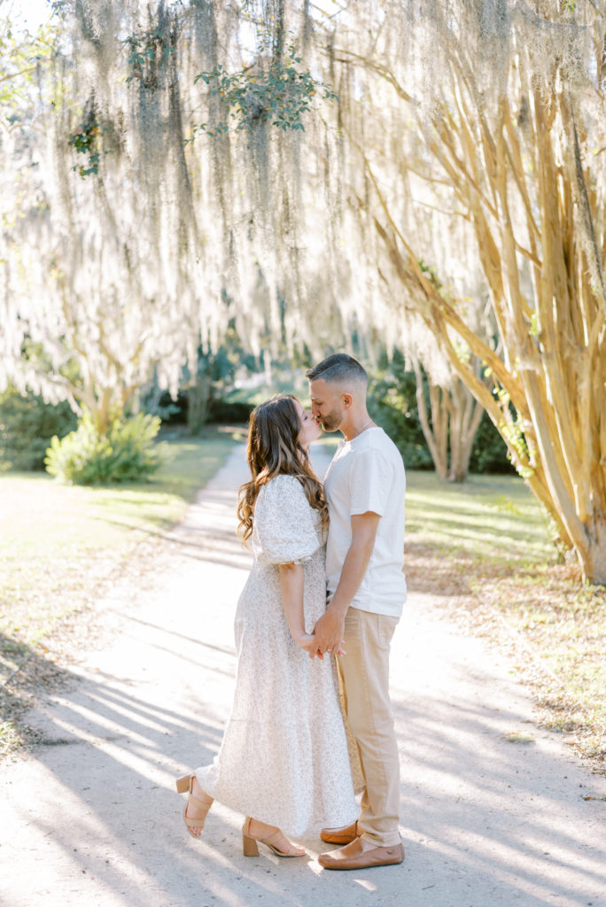 Married couple kissing under crepe myrtles and Spanish moss in Hampton Park at sunset