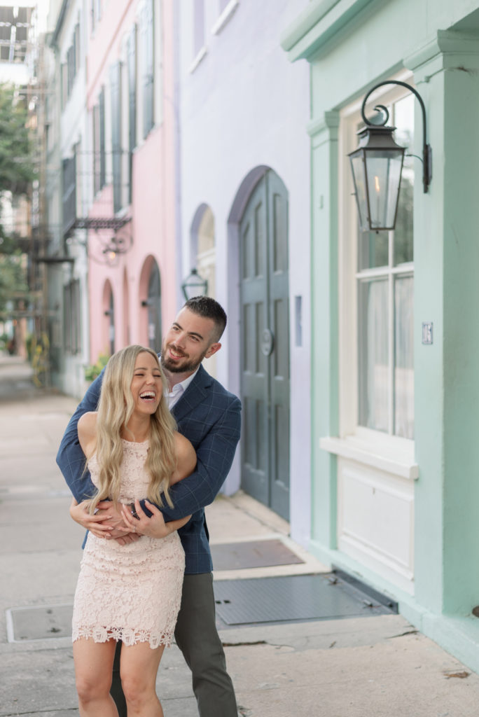 Engaged man and woman hugging on Rainbow Row in Charleston South Carolina wearing white dress and blue suit coat