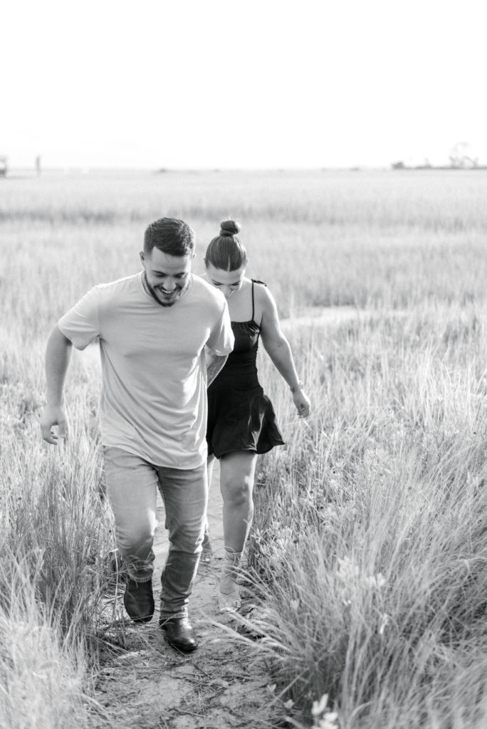 black and white image of engaged couple running in the Shem Creek marsh at sunset in Charleston South Carolina