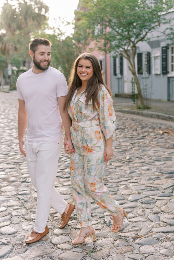 Engaged couple holding hands and walking in cobblestone at sunrise in Charleston South Carolina