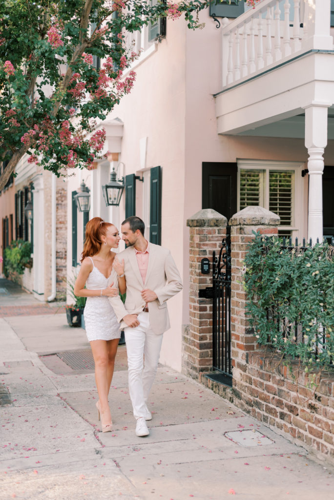Couple walking down the street together in late August in Charleston under pink crepe myrtle