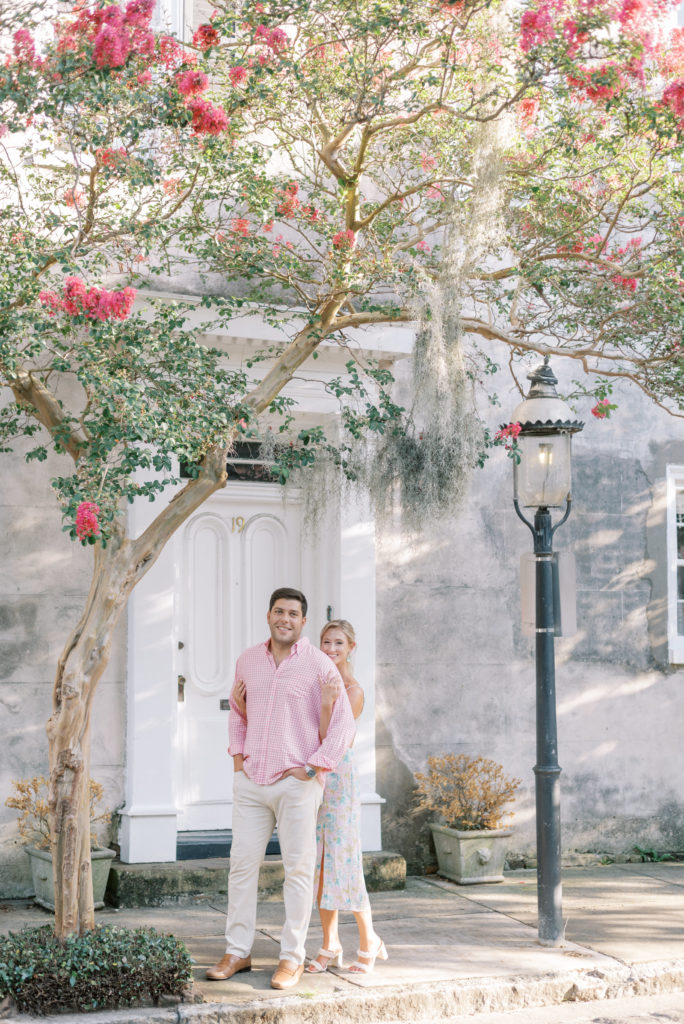Engaged couple wearing pastel pink hugging under pink crepe myrtle in Charleston