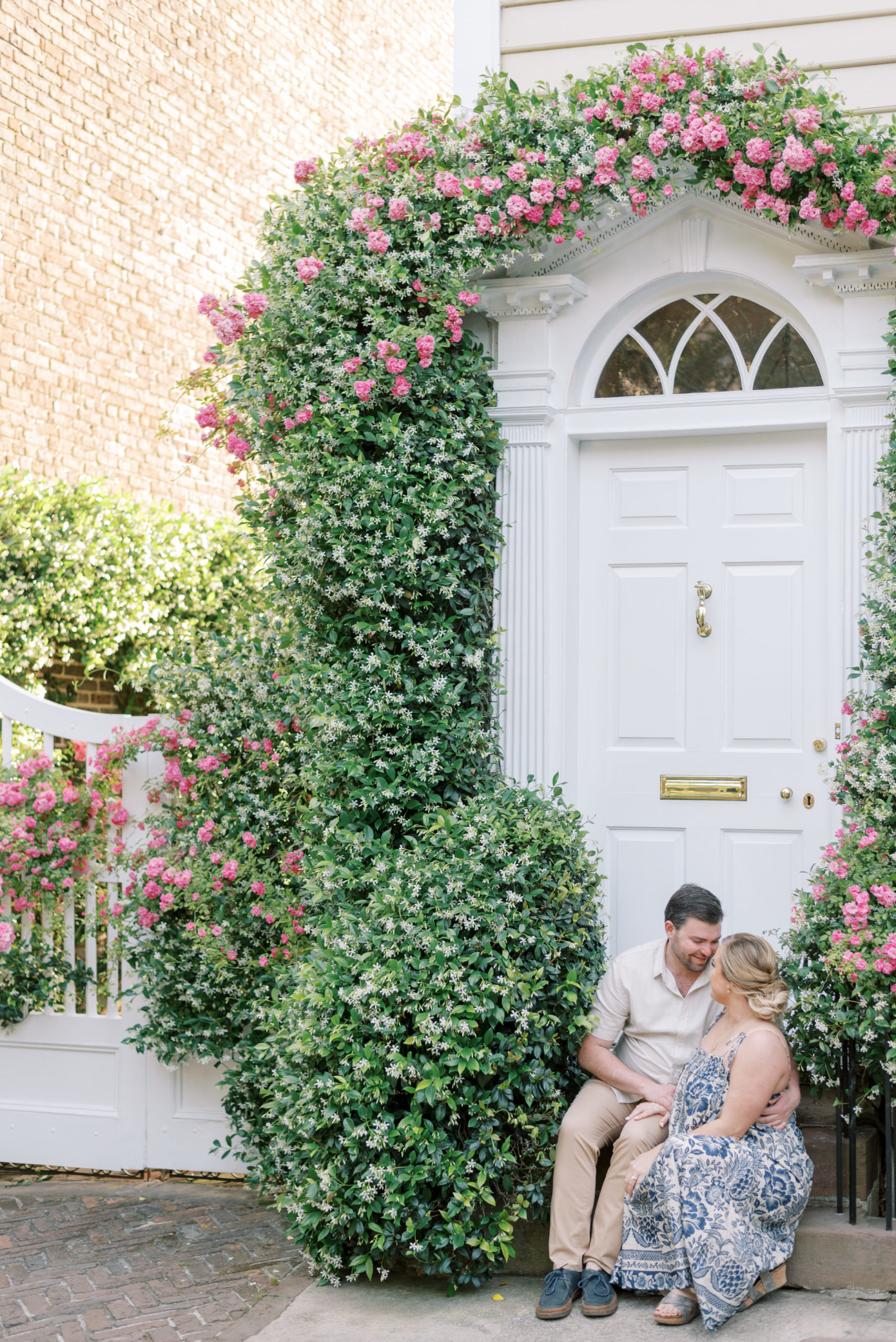 Couple sitting on a step with pink and white flowers and a white gate