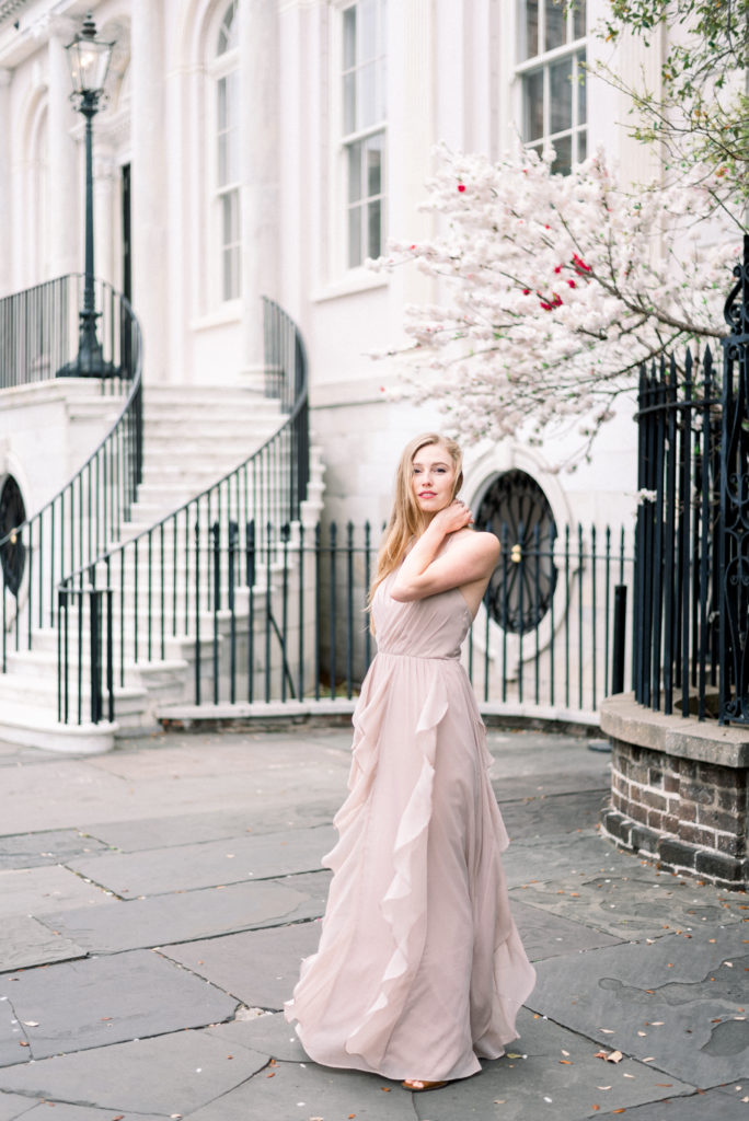 blonde woman in lavender dress in front of white stone building and flowers in March photographed by Kelsey Halm Photography