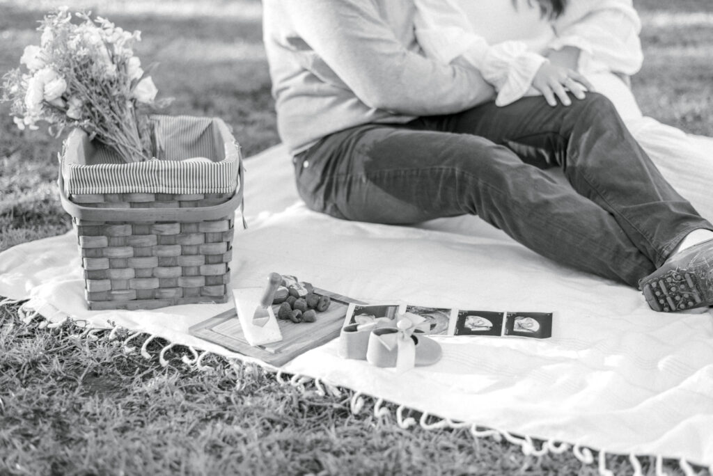 Black and white photo of expectant parents on a blanket having a picnic