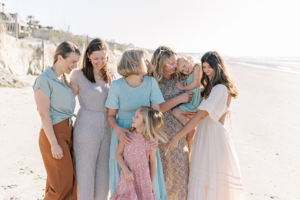 A joyful and heartwarming image of a mother surrounded by her daughters-in-law and their children, all laughing together on the beautiful Isle of Palms beach during their family vacation. The sun is shining brightly, casting a warm and happy glow on the group as they enjoy each other's company and the stunning ocean view. The mother is beaming with love and pride as she embraces her family, creating a beautiful and lasting memory.