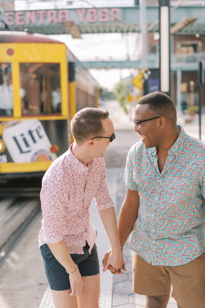 gay couple hold hands and laugh together while waiting for the trolley