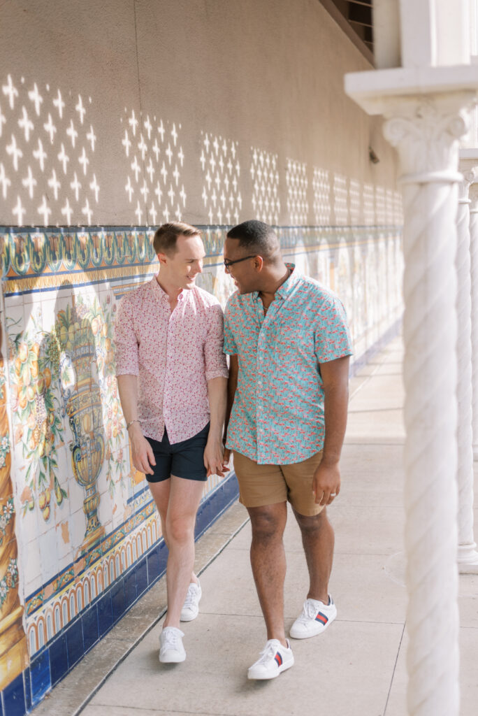 couple holds hands and walk together past tile wall