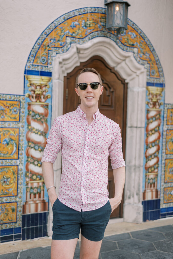 portrait of a man in a colorful shirt and sunglasses in front of bright tile wall and wood door