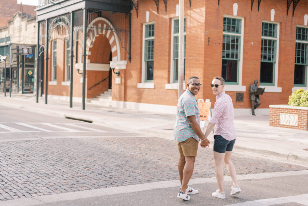 Couple smile back at the camera in front of red brick building