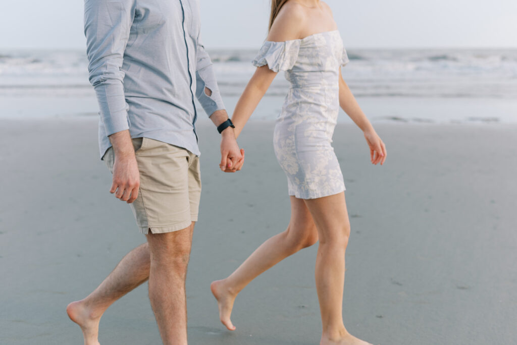 couple holding hands and walking in front of the water at the beach