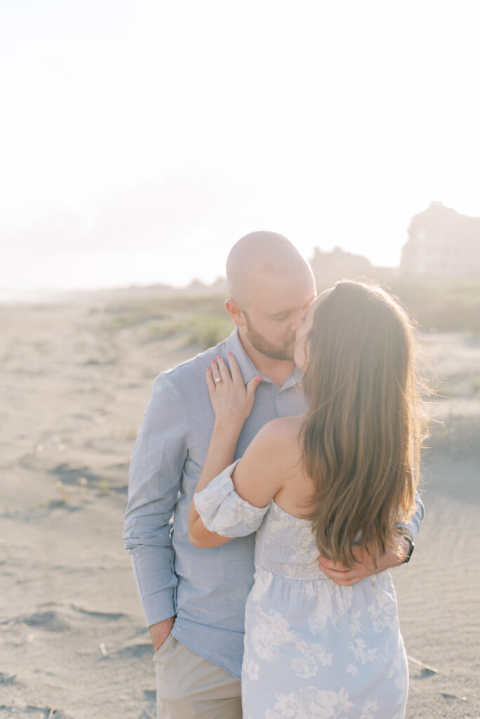 engaged couple kiss by the sand dunes at sunset on the beach