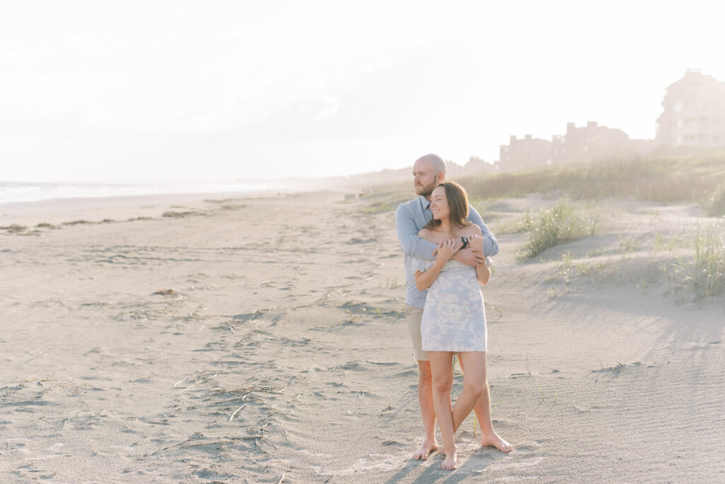 engaged couple hug and lean on each other by the dunes at sunset on kiawah island