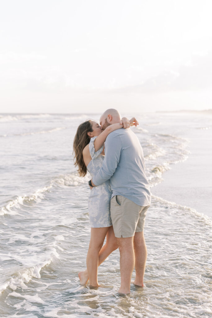 engaged couple hug and kiss and stand in the water on the beach at kiawah