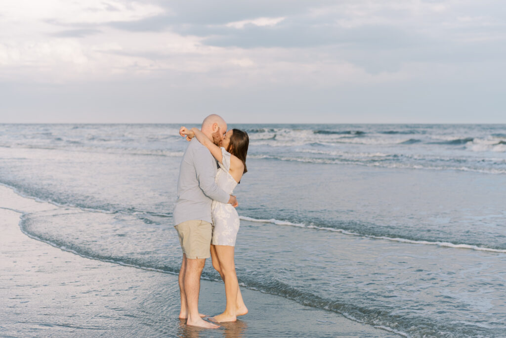 engaged couple kiss in the ocean at sunset