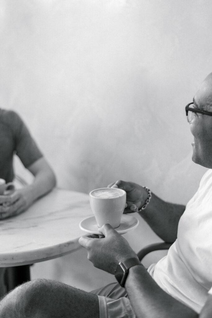 man sits and enjoys a latte with his partner at a cafe table 