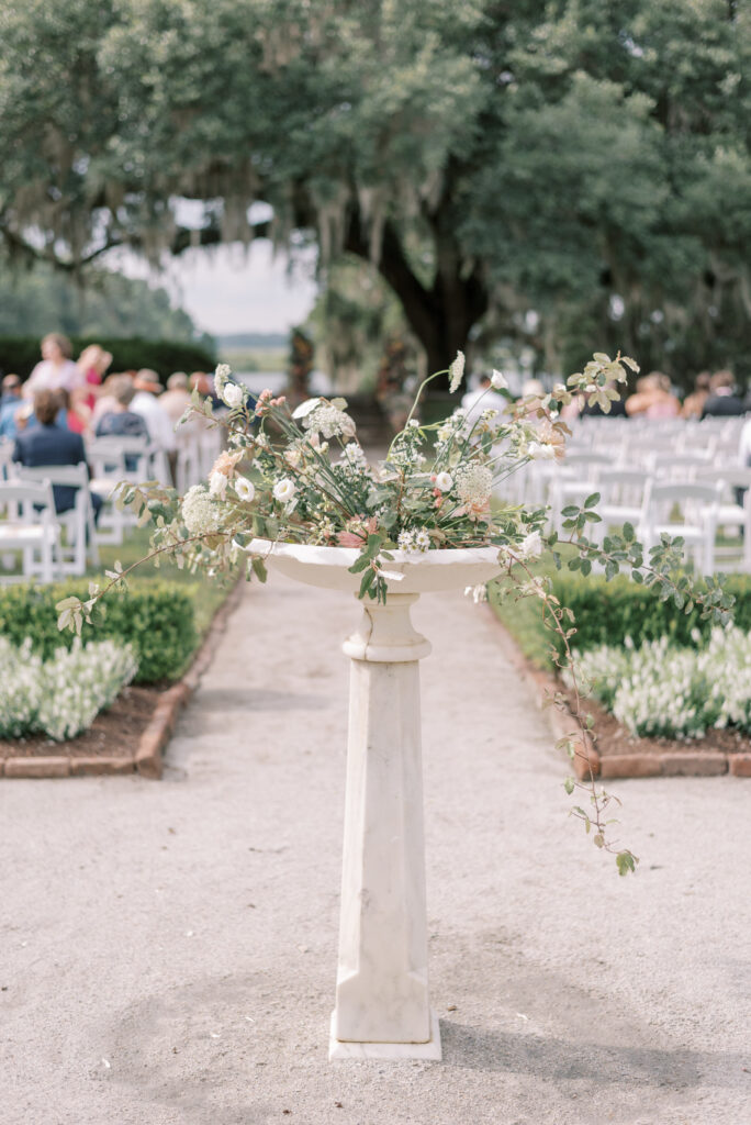 Sundial with flowers draping out at the head of a wedding aisle 