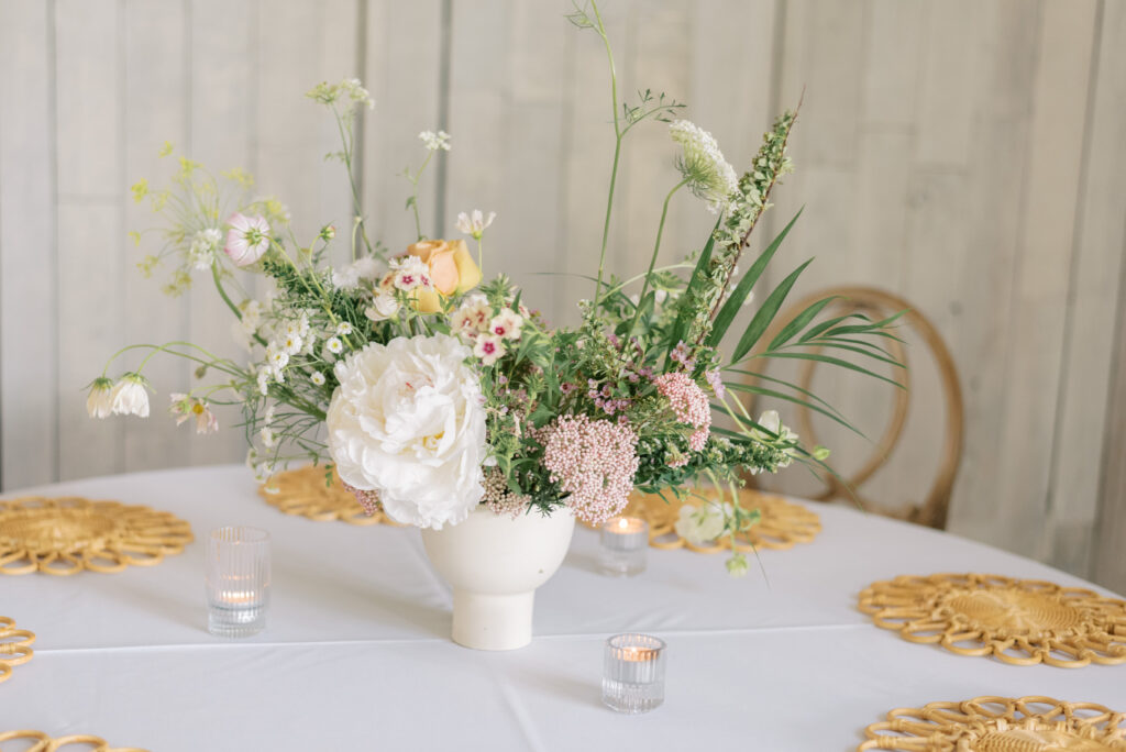 pastel summer florals in a white urn at a reception table with rattan place chargers