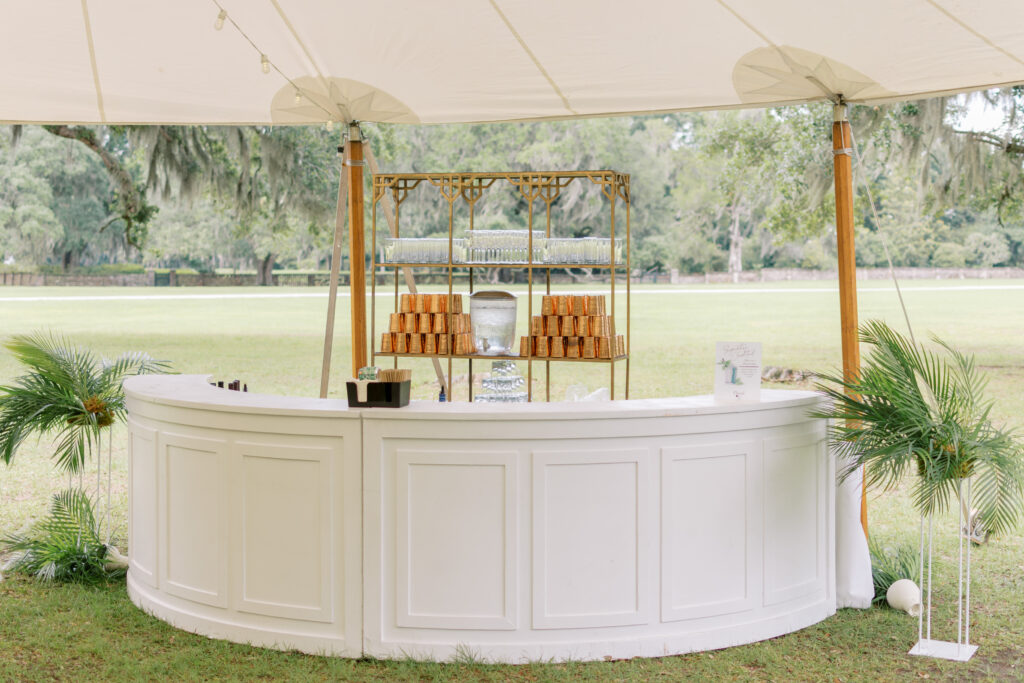 White bar with copper glassware under a sailcloth reception tent