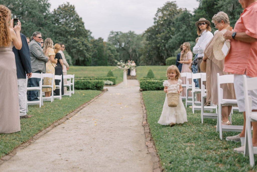 Flower girl carrying a small flower basket walks down the aisle at Middleton Place 