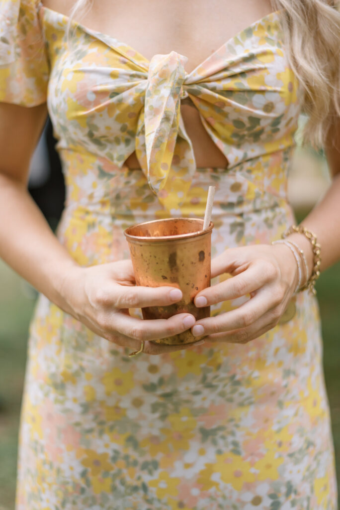 Woman in a yellow floral dress holds a copper cup with moscow mule 