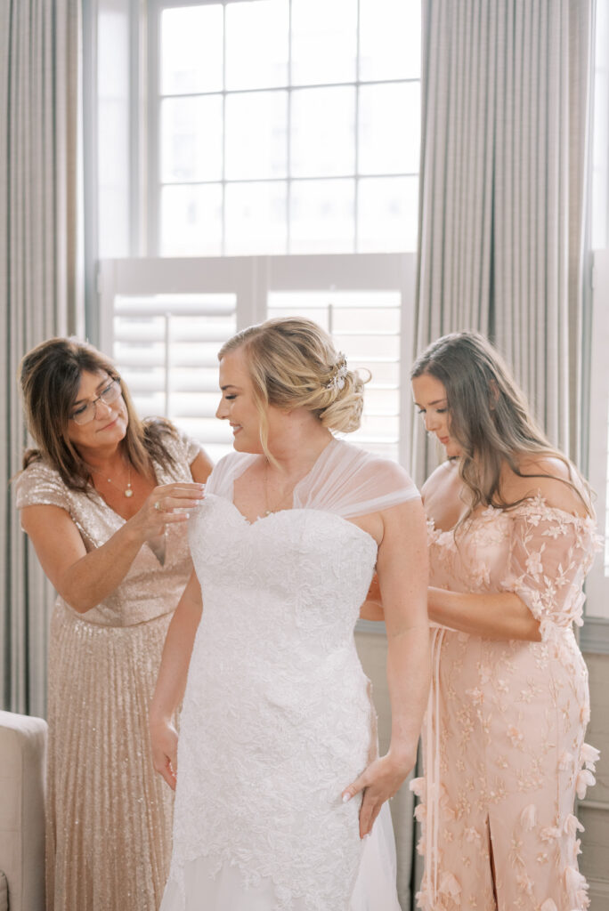 Bride getting into her Anne Barge dress with the help of her mother and sister