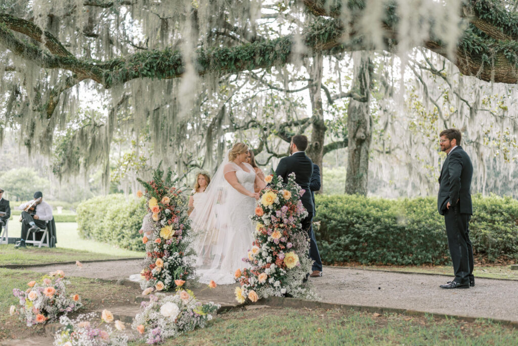 Bride and groom stand hand in hand at their wedding ceremony under live oaks and spanish moss