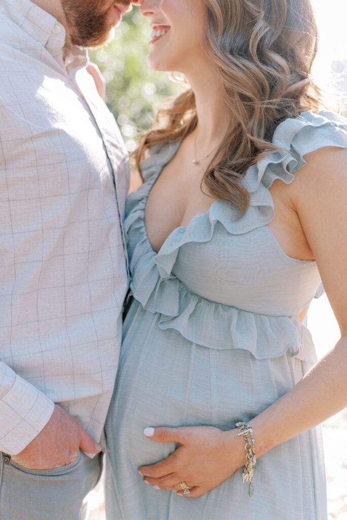 close up of a man and woman standing close together smiling while she has her hand on her pregnant belly