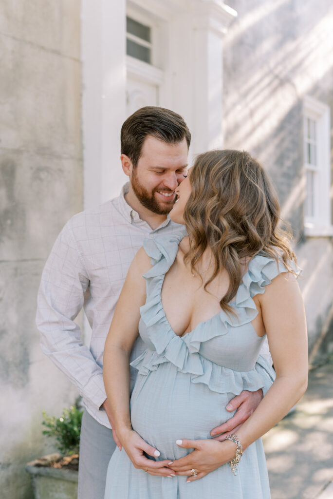 man wraps his arms around his wife and she leans back into him with their hands on her pregnant stomach