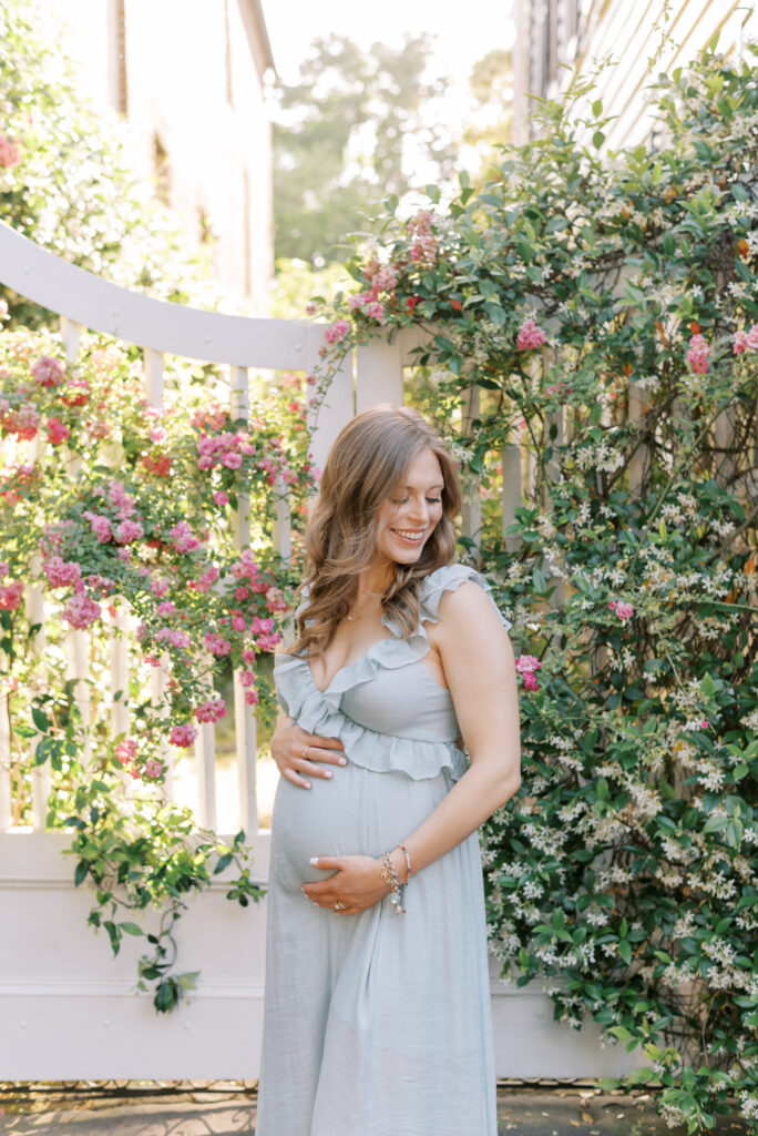 Maternity photo of a woman in front of a white charleston gate with jasmine and pink flowers