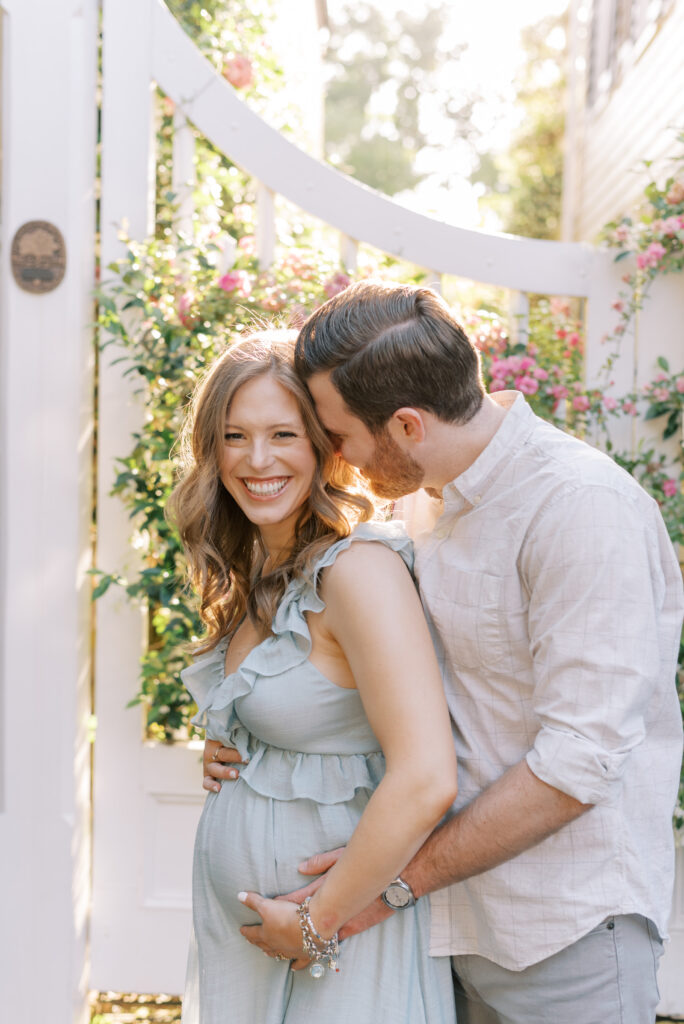 husband and wife laughing together while he kisses her cheek in front of a floral gate in Charleston