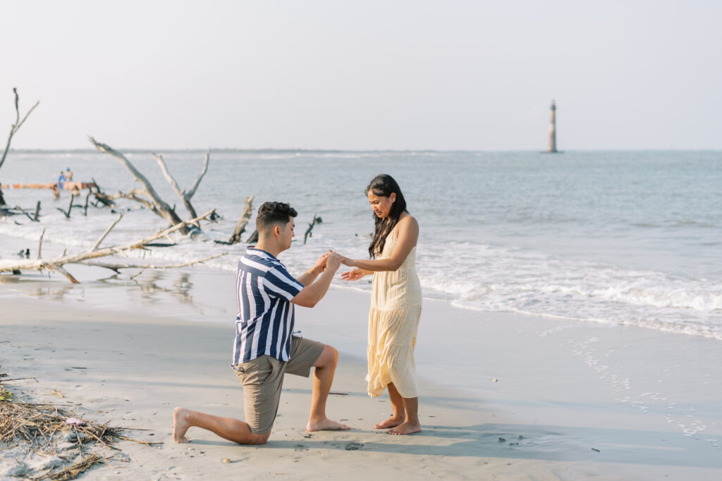 man puts a ring on his fiance's hand after proposing on the beach