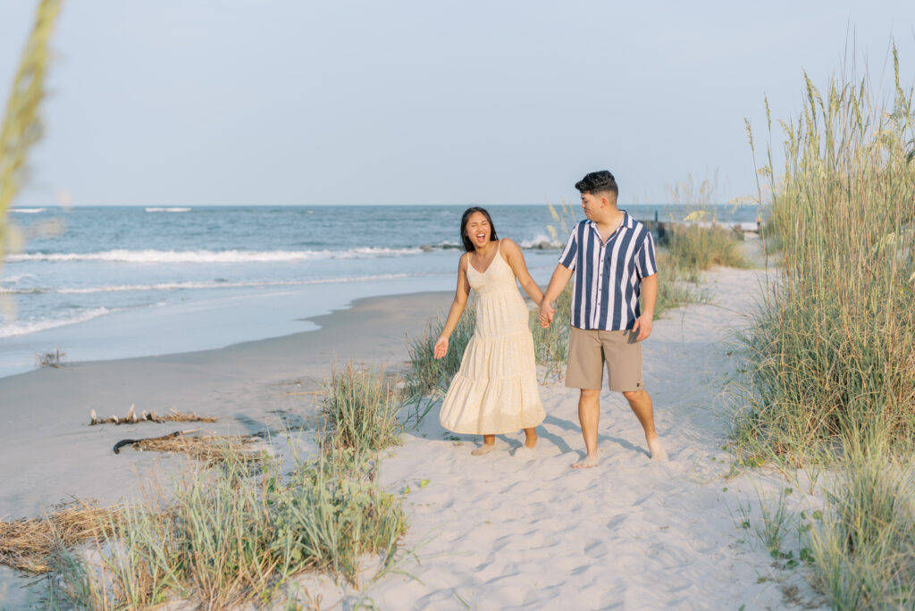 couple laugh together walking along a beach path