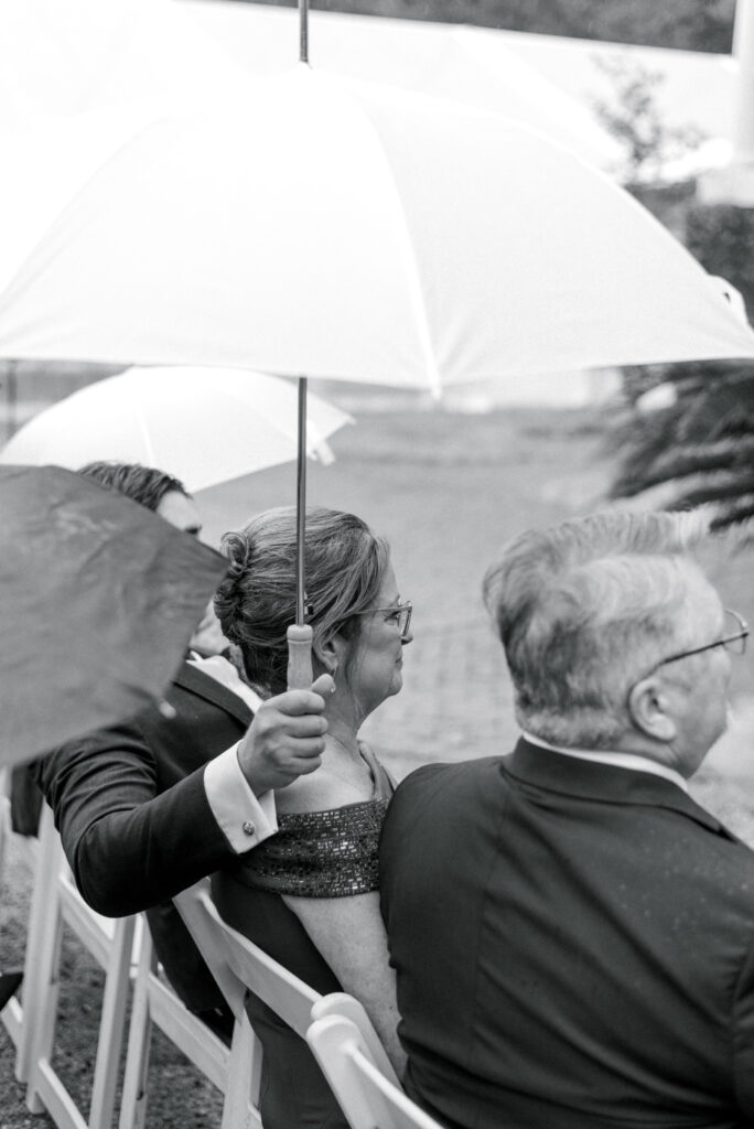 Son holds umbrella over his mother during wedding ceremony