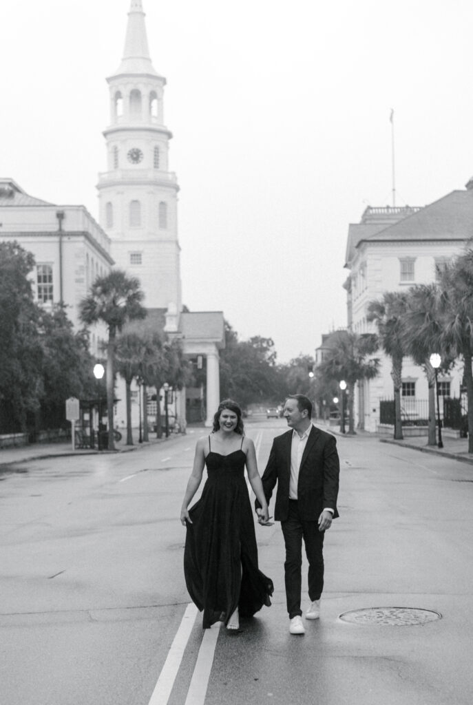 Black and white image of an engaged couple walking in the middle of the street in Charleston South Carolina