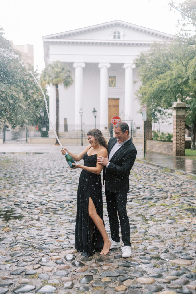 Engaged couple pop a champagne bottle on a cobblestone street in Charleston