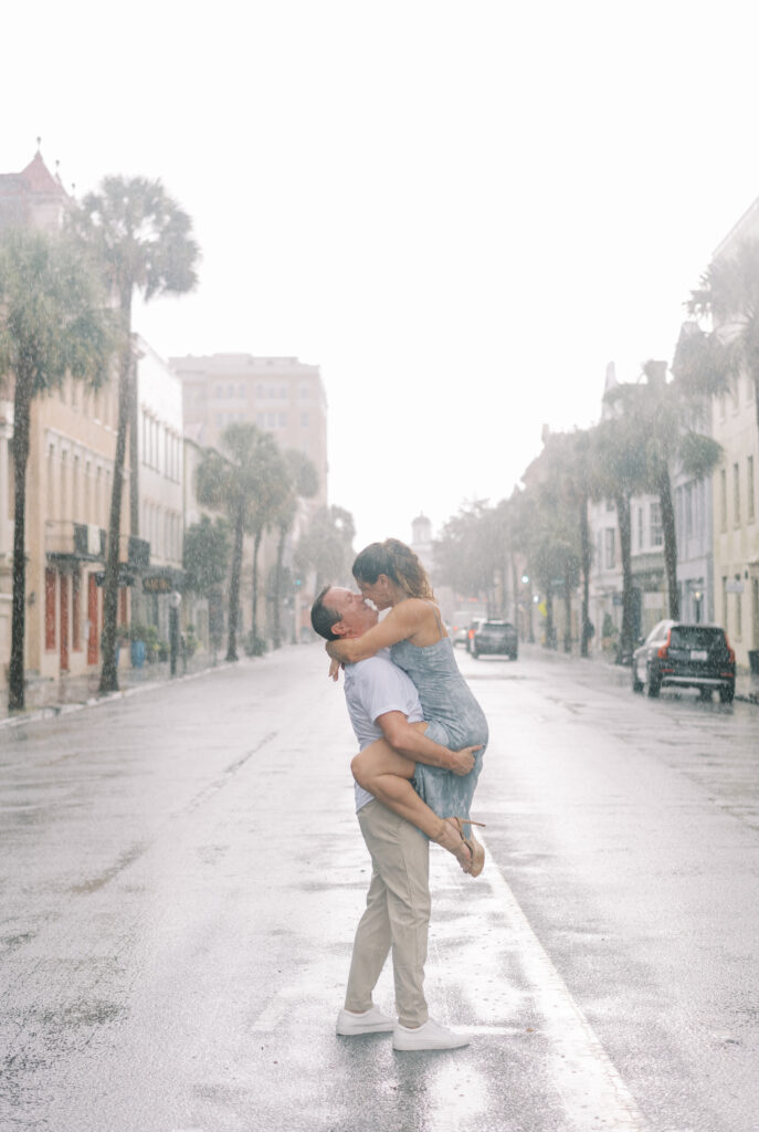 Man holds his fiancé in the middle of the street for a kiss during a rain storm