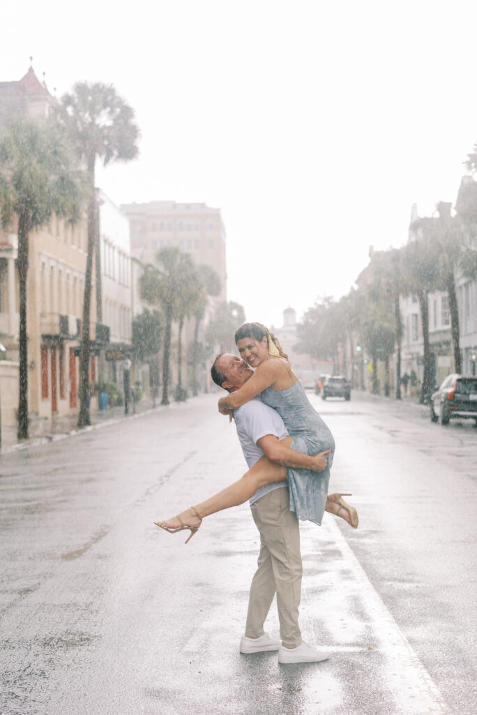 couple laugh together as the man holds his fiancé in the middle of Broad st during a rain storm