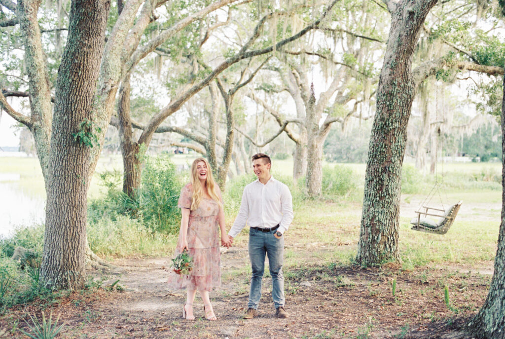 couple holds hands and laughs under the oak trees