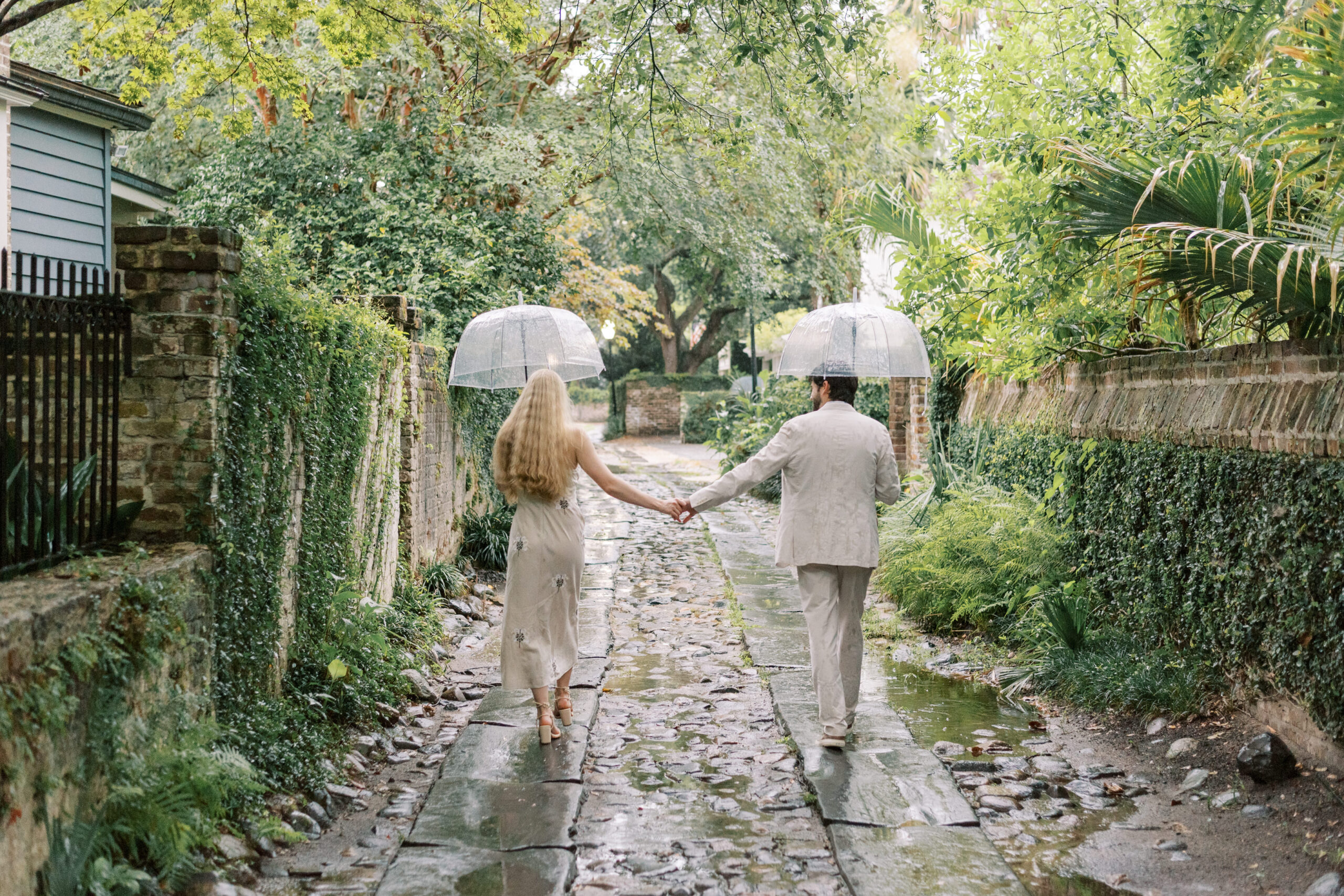 Engaged couple walk through rainy cobblestone alley in Charleston SC