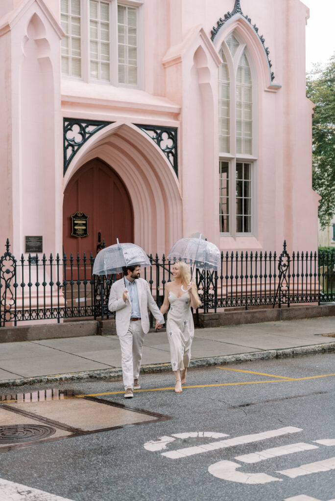 Couple hold hands and cross the street in front of the French Huguenot Church in Charleston 
