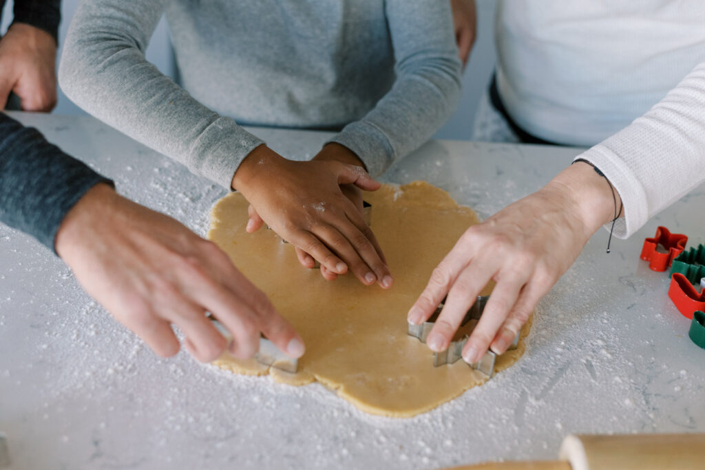 close up of family's hands as they use cookie cutters to cut cookie dough