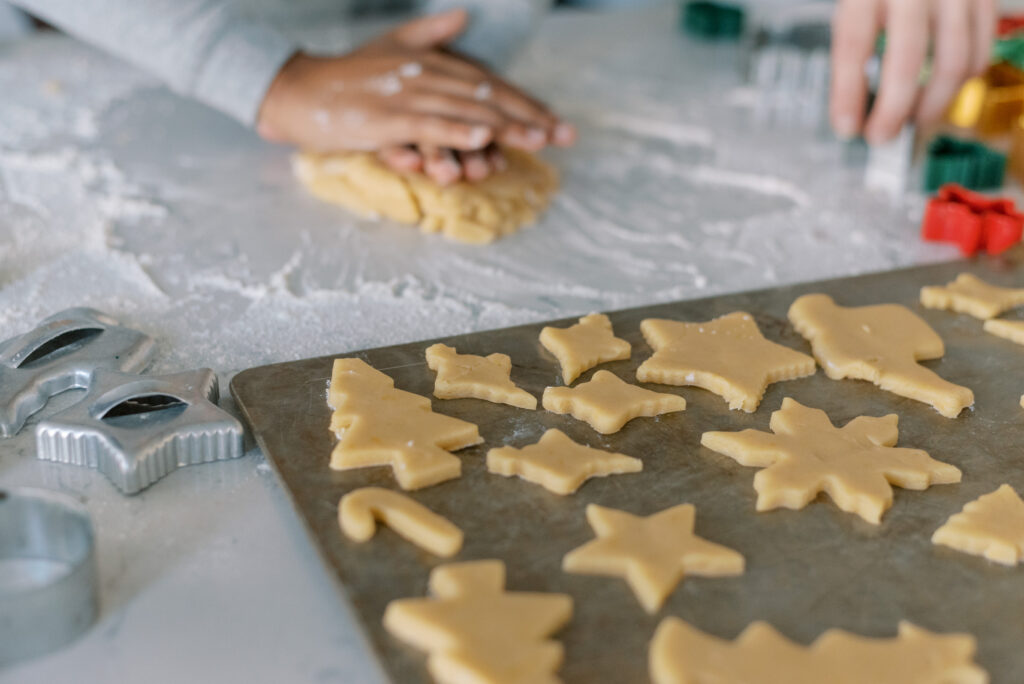 christmas cookies on a tray with hands rolling dough in the background