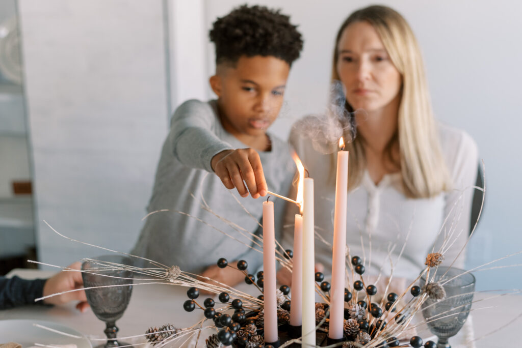 child lights candles in a neutral holiday centerpiece while mother watches