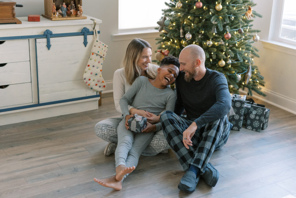 family cuddles together sitting on the floor in front of their christmas tree