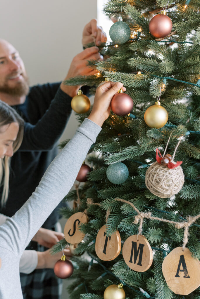 family decorates the christmas tree with blush and gold and green ornaments and wooden christmas sign on twine