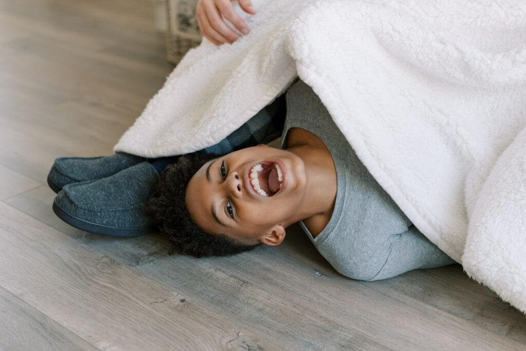 boy has a huge laugh while laying under a blanket by his dad's feet