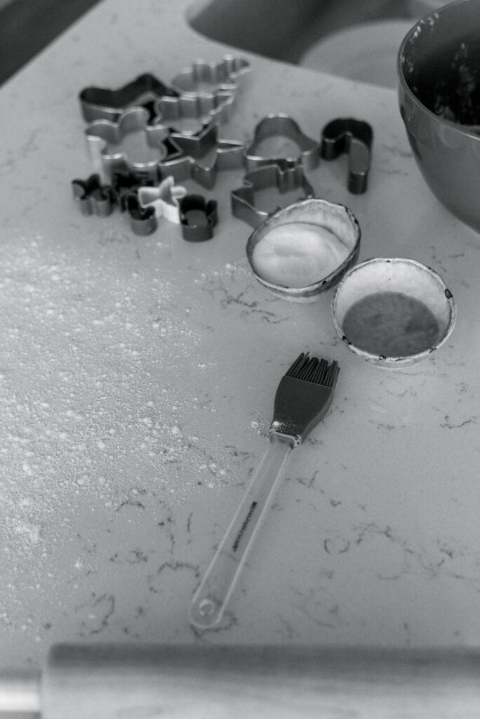 black and white image of cookie cutters and baking tools scattered on a marble countertop